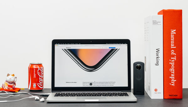 A-creative-workspace-showcasing-an-open-MacBook-Pro-laptop-next-to-headphones-a-Coke-and-several-books-on-Working-and-Typography