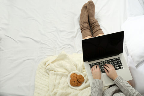 Woman-eating-cookies-in-bed-with-MacBook-laptop 