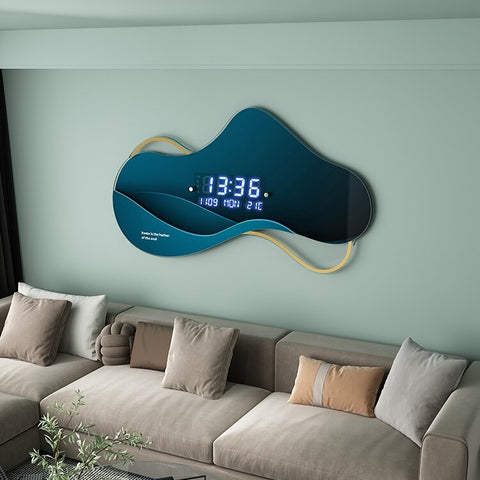 An unusual shaped wall clock called an Asymmetrical Dream Clock. The main component of the clock is greenish blue and is shaped similar to a cloud. The time reads 13:36pm and the clock is hung on a green wall above a light brown lounge with cushions on it.