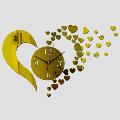 A gold flying heart clock. The clock is in the shape of a love heart, with a dial in the centre. The right hand side of the clock looks like it is shattered into lots of tiny little gold hearts flying away across the wall.