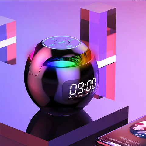 A side profile of a sphere shaped bedside electronic alarm clock which reads 9:00am. There are touch buttons on top and colors throughout the sphere which sits on a luminous table and purple colored background.