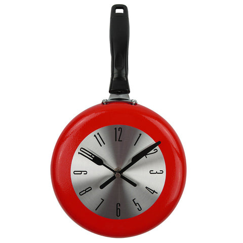 A frying pan kitchen wall clock. The clock is in the shape of a frying pan, the pan is red and it has a black handle. The hands are a fork and knife which reads 10:10am