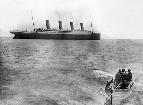 An image from 1912 of the Titanic out to sea. There is a smaller white row boat at the foreground of the image