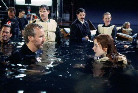 Behind the scenes from Titanic with Director James Cameron and actress Kate Winslet talking while in the water. The are other actors in the background.