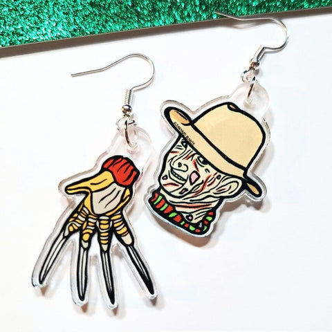 A pair of earrings inspired by the movie A Nightmare on Elm Street. One earring features Freddy Krueger's face and the other is of his glove made from knives. The earrings are on a white background.
