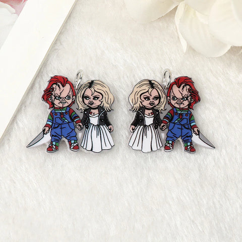 A pair of stud earrings inspired by the movie franchise called Child’s Play. Each earring features the doll called Chucky holding a knife in one hand and in the other hand and he is holding the hand of the Bride of Chucky, his girlfriend the movies. The earrings are in the palm of a persons hand showing them close up.