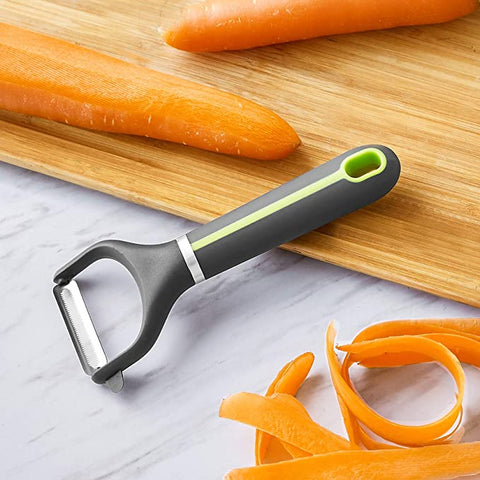 A grey and green julienne peeler resting on a chopping board with two peeled carrots nearby