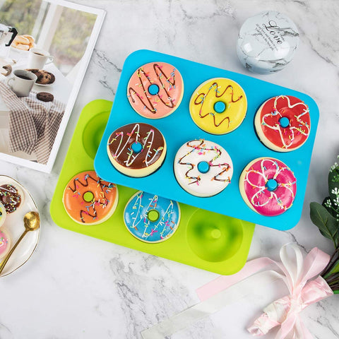 One green and one blue silicone donut molds with colorful donuts inside the molds resting on a kitchen bench