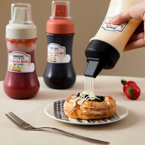 A five hole squeeze bottle filled with custard squirting 5 rows of custard on a danish. There are 2 other 5 hole bottles behind this.