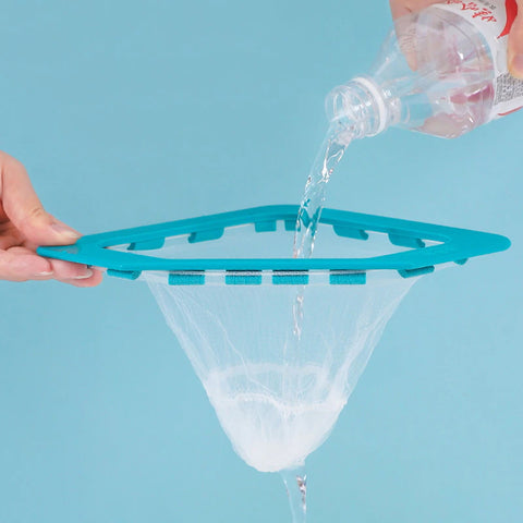 A hand holding a triangle sink strainer with another hand pouring water from a bottle in the strainer.