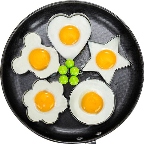 A five piece stainless steel set of molds used for frying eggs in different shapes including, circle, star, flower, heart and Mickey Mouse. The molds have fried eggs in them inside a frying pan.