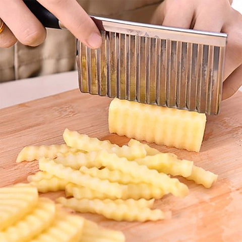 A wavy shaped stainless steel knife slicing up a potato into crinkle cut shapes.