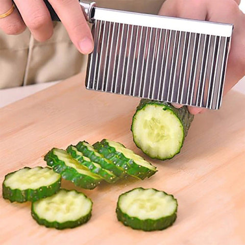 A wavy shaped stainless steel knife slicing up a cucumber  into crinkle cut circular shapes.