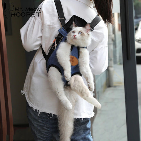 A white cat strapped into a cat harness backpack being carried on a persons back while outdoors.