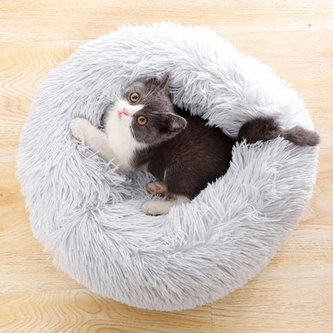 A black grey and white kitten resting in a super fluffy grey cat bed