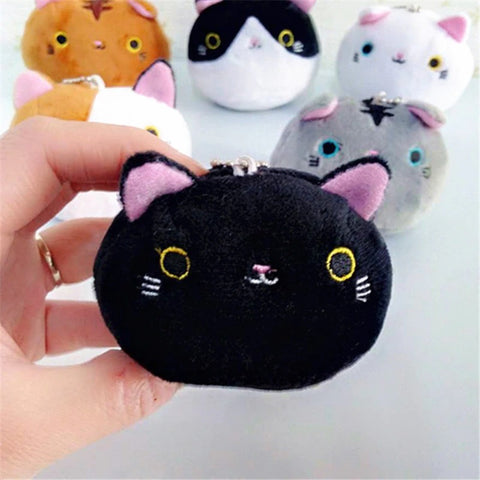 A hand is squashing a cute and fluffy cat head keychain. In the background are different colored keychains which also feature cats heads.