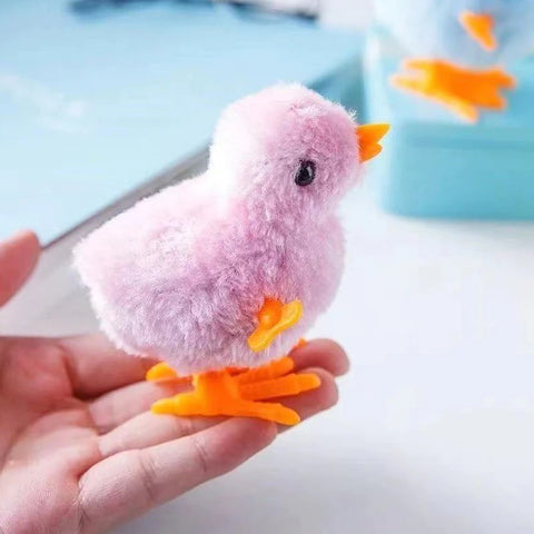 A pink cat toy wind up chicken resting on a persons fingertips