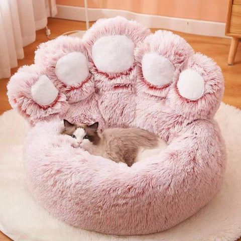 A giant pink cat bed which is shaped as a big cat paw, there is a cat resting in the bed.