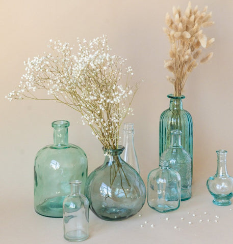 8 glass vases of different shapes and sizes. Two of the vases have dried flowers in them.