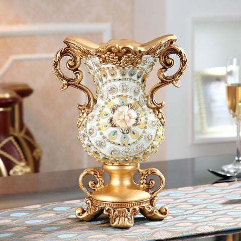 A lavish white and gold antique-looking vase with a floral design in the centre and gold twin handles on the side. The vase is empty.