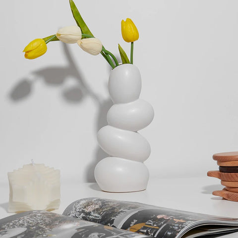 An odd shaped vase which looks like 4 eggs stacked on top of each other and are balancing altogether. Inside the vase are 2 yellow and 2 white tulips.