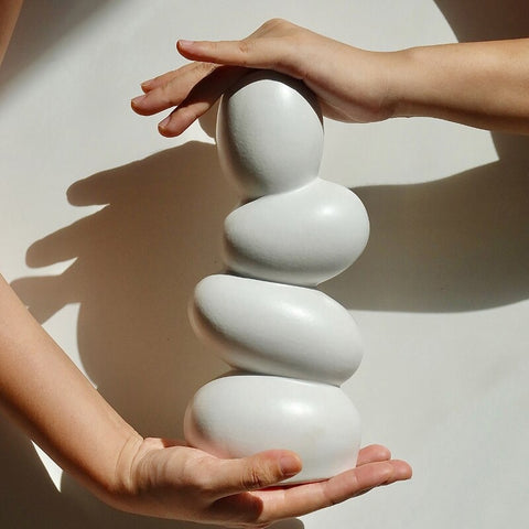 An odd shaped vase which looks like 4 eggs are stacked on top of each other and are balancing altogether. A person’s hands are holding the vase on each end showing the size.