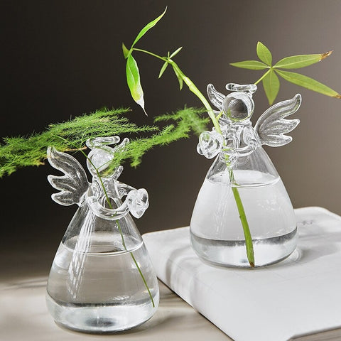 Two cute glass vases in the shape of angels with wings and halos. Each vase has a small decorative green plant in it.