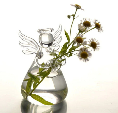 A cute glass vase in the shape of an angel with wings and a halo. The vase has tiny daises in it.