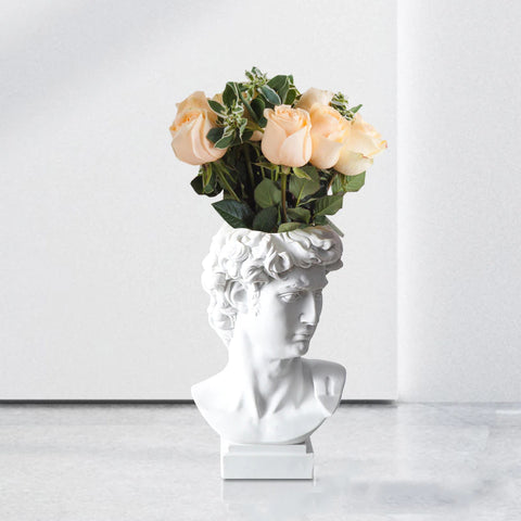 A vase of the statue of David but only his head with an opening in the top for flowers. There are apricot colored roses in the vase