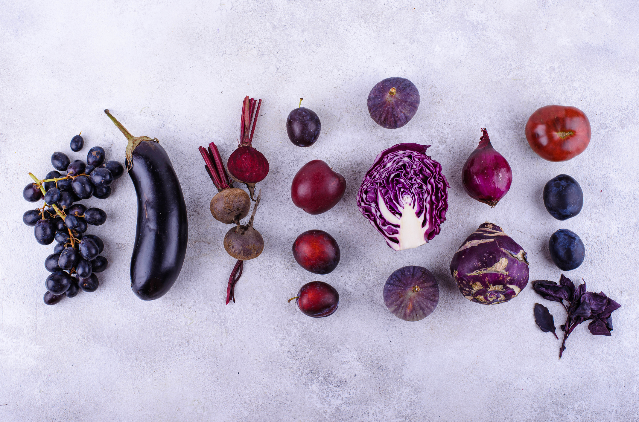 Overhead image of purple produce like eggplant, grapes, cabbage, figs, plums and beets