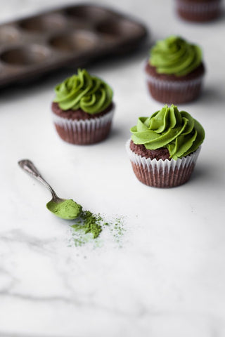 chocolate cupcakes iced with matcha frosting and a spoon with matcha powder in foreground
