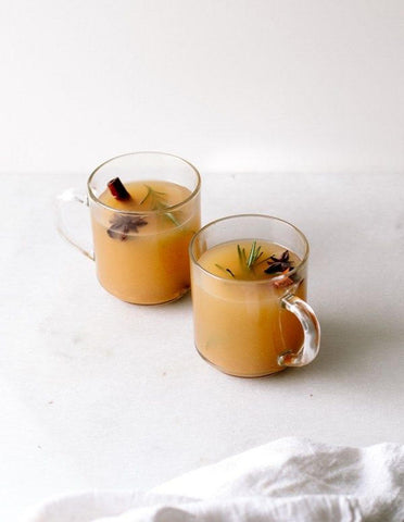 two glass mugs of apple cider with cinnamon sticks and cloves
