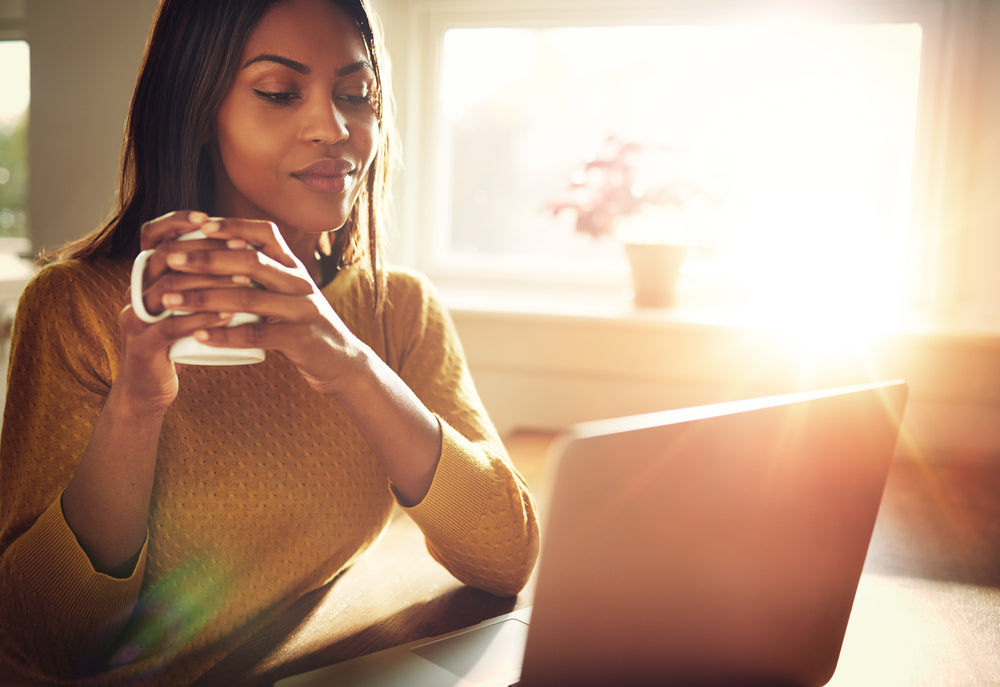 Woman in yellow sweater working and drinking a warm beverage