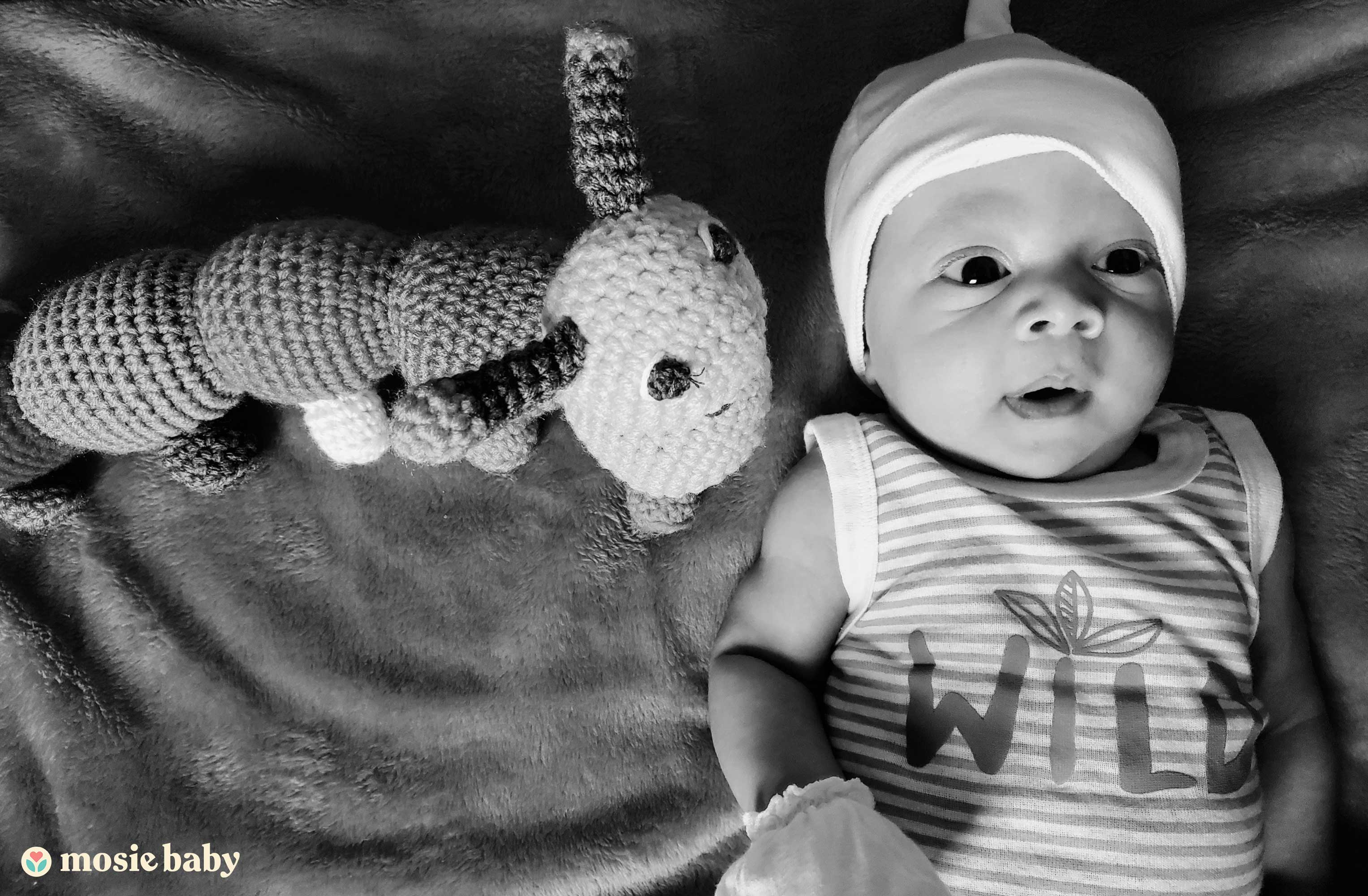 Black and white photo of a baby with a toy stuffed animal