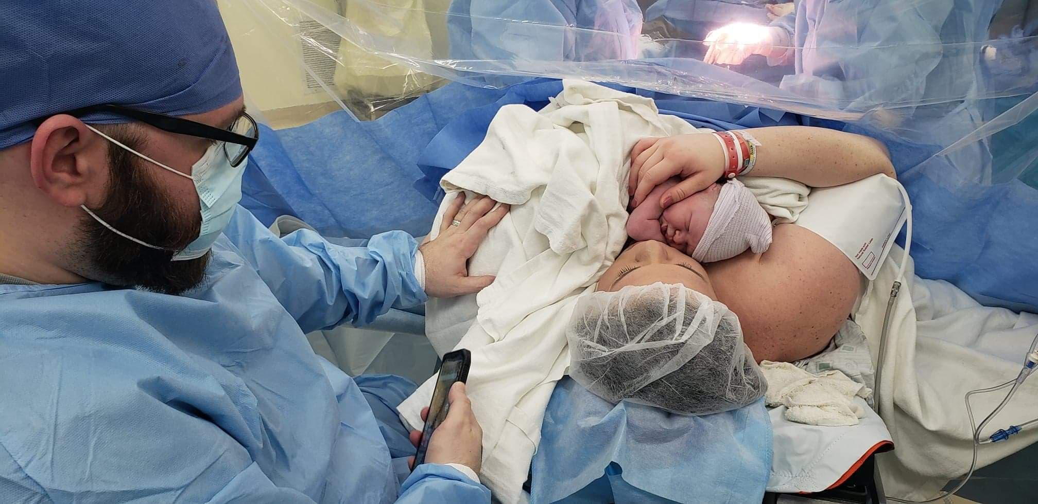 Woman holds newborn after c-section. Man rests hand on her shoulder