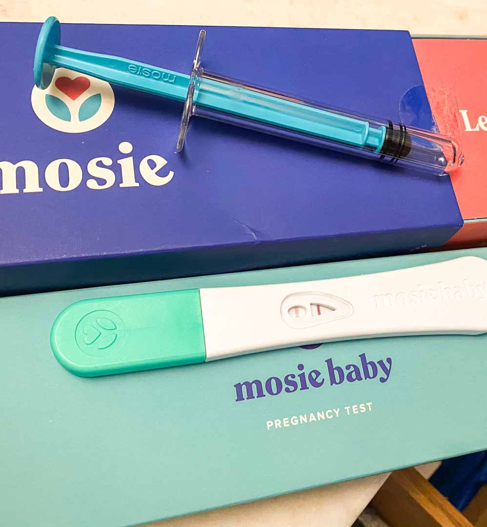 Mosie syringe on top of the Mosie Kit box and positive pregnancy test stick on top of box.