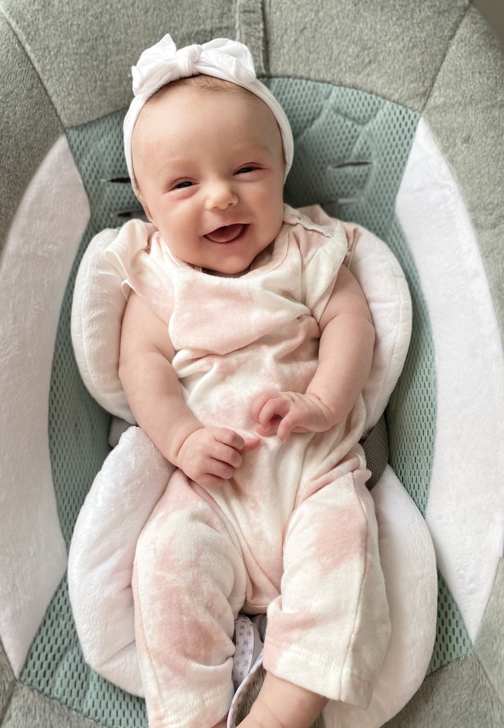 Mosie Baby girl sitting up and smiling with hair band in her hair.