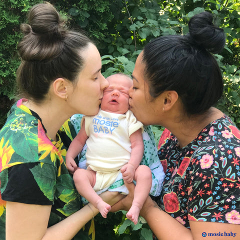 two lesbian moms kissing their newborn mosie baby