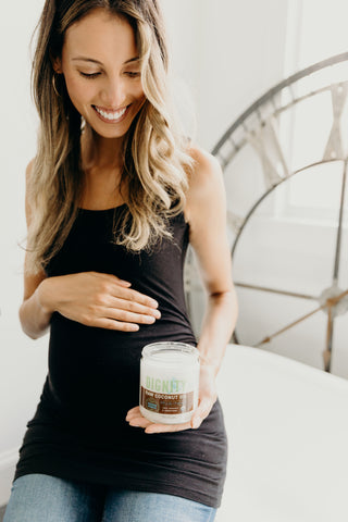 A pregnant mom is holding out a jar of coconut oil