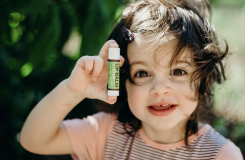 A little girl smiles as she holds up a tub of Dignity Coconuts lip balm to show off its all natural ingredients.