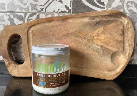 A jar of Dignity Coconut coconut oil with a freshly cleaned wood cutting board