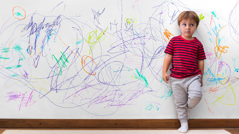 Kid leans against a wall that has crayon marks all over it