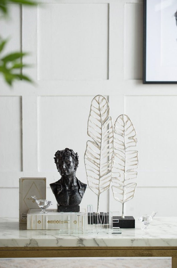 two silver feather outline sculptures are featured on a shelf alongside other trinkets