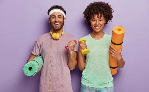 Two friends posing in front of purple wall with exercise equipment