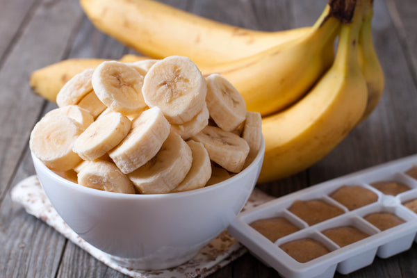 Banana slices in a bowl with full bananas behind
