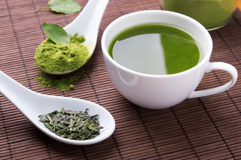 Green Tea powder and loose leaves with fresh brewed tea in a white tea cup