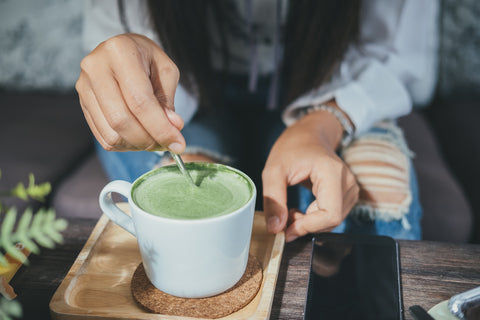 girl stirring hot matcha green tea in a white mug