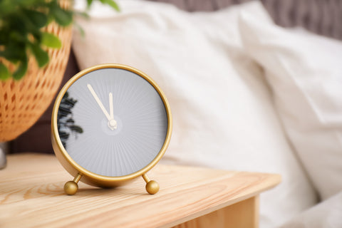 analog clock next to a bed setting a sleep schedule