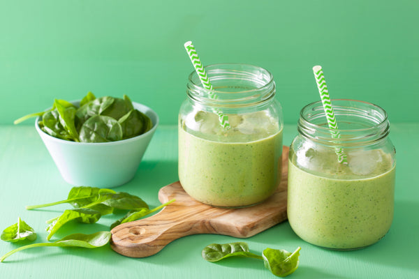 2 cups of spinach green smoothies with leaves of spinach around