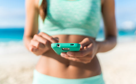 woman checking phone on the beach wearing work out clothes